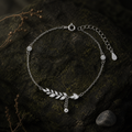 Silver wheat charm bracelet arranged on mossed stone