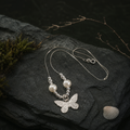 Etched silver butterfly pendant with two round pearls resting on mossed slate