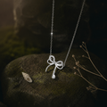 Bow-shaped silver pendant on mossed stone beside small shells