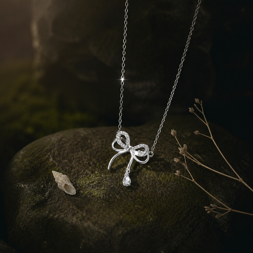 Bow-shaped silver pendant on mossed stone beside small shells