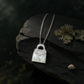 Small mother-of-pearl bag pendant resting on the edge of slate with lichen and a small shell