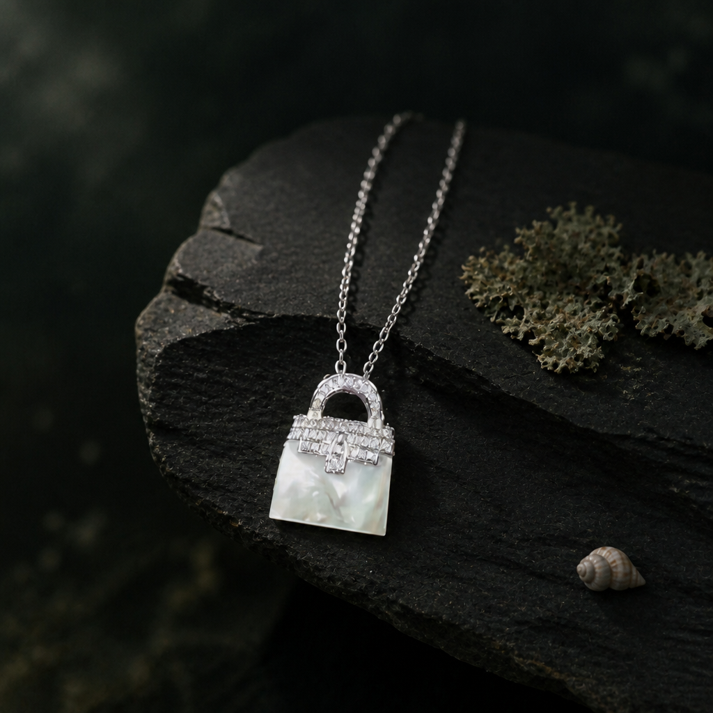 Small mother-of-pearl bag pendant resting on the edge of slate with lichen and a small shell