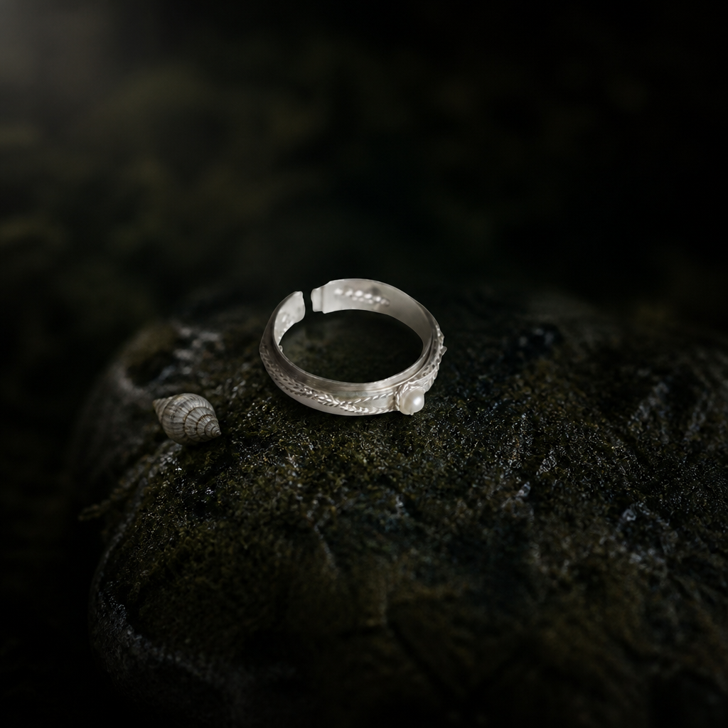 Twisted wire ring holding a shell pearl on mossed stone beside a small shell