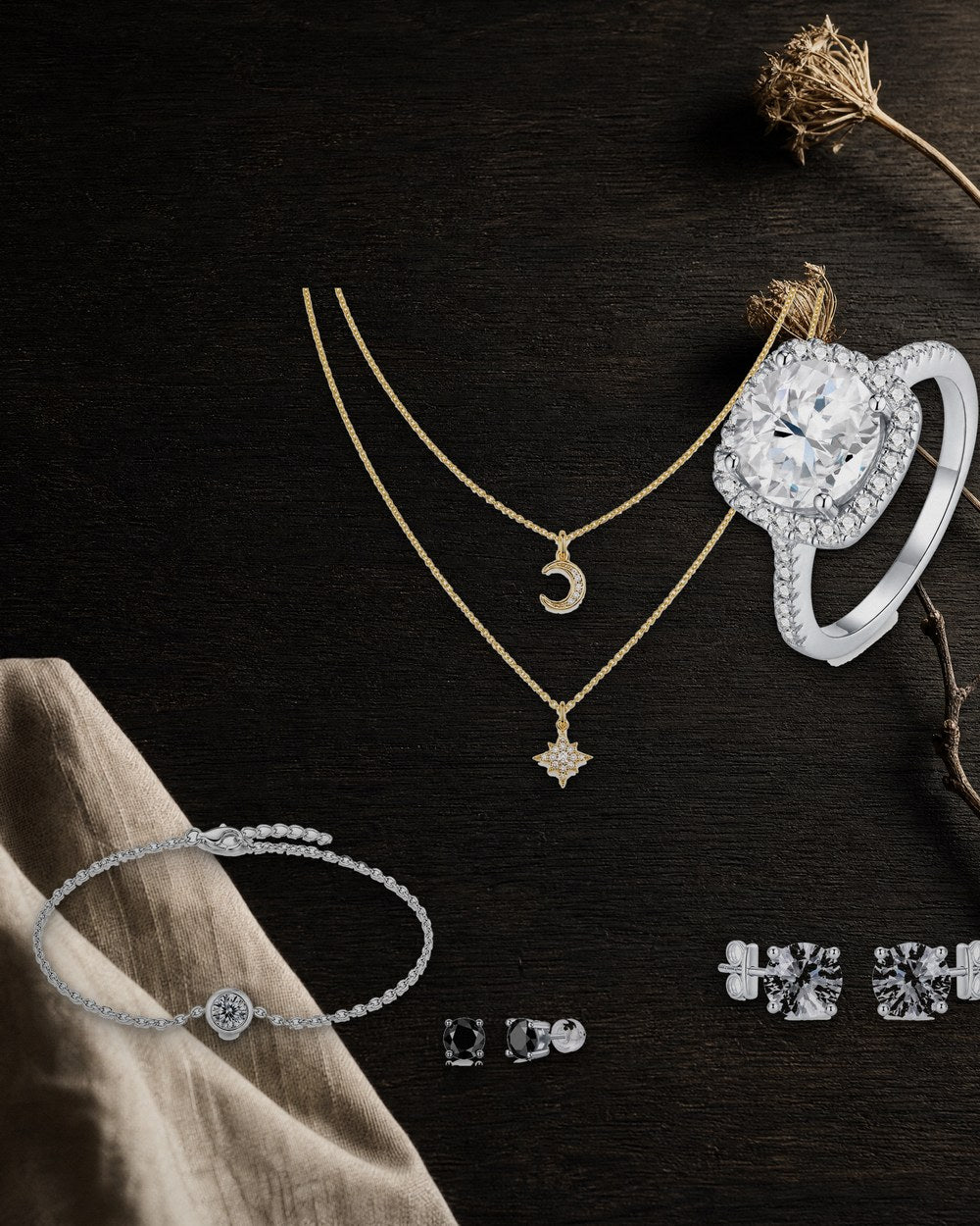 A gold-plated layered moissanite necklace with crescent and star pendants, a moissanite bracelet, a moissanite ring and white and black moissanite ear studs arranged on dark wood.